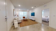 This contemporary single-floor residence is thoughtfully designed with a clean, minimalist aesthetic that emphasizes open space and natural light. Polished concrete flooring flows through the main living areas, lending an industrial-modern character that ties the home together seamlessly.

The open-concept living area is bright and airy, anchored by large sliding glass doors that invite abundant natural light and provide outdoor views. The space comfortably accommodates both a seating area and a dedicated lounge nook, making it ideal for relaxing or entertaining.

The kitchen is a standout feature, outfitted with crisp white cabinetry extending to the ceiling for generous storage, stainless steel appliances including a refrigerator, range, and built-in microwave, and a central island with a white quartz countertop offering additional prep and seating space.

The primary bedroom is serene and well-proportioned, flanked by two windows that bathe the room in soft, diffused light. It is complemented by a spacious walk-in closet with custom shelving and hanging rods, and a private en-suite bathroom featuring a dual-sink vanity with white cabinetry, a large mirror, and a glass-enclosed shower. A second bedroom offers corner windows and plush carpeting for added comfort. A dedicated laundry area completes this well-appointed home.