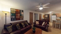 Located at 1796E E Parkshore Dr in Fayetteville, Arkansas, this single-story residence offers a thoughtfully organized layout across several distinct living spaces. The living room serves as a central gathering area, finished with carpet flooring and a textured ceiling overhead. Ceiling fans are present throughout, providing both function and a consistent design element across rooms. Large wall art adds visual character to the living space, which is anchored by a wood coffee table and flows naturally toward the bedroom hallway.

The kitchen is well-equipped with warm oak cabinetry extending to the ceiling, offering generous storage. Appliances include a range, dishwasher, refrigerator, and microwave. Light tile flooring and light countertops keep the space bright, while a peninsula provides additional prep and serving space adjacent to the dining area. The dining room accommodates a round table and connects conveniently to an in-unit laundry closet, a practical and notable feature.

Two carpeted bedrooms each include ceiling fans, windows with blinds for natural light control, and ample dresser storage. The bathroom features tile flooring and a shower-tub combination with sliding glass doors. Throughout, the residence maintains a cohesive, functional character suited to comfortable everyday living.