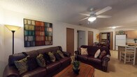 Located at 1796E E Parkshore Dr in Fayetteville, Arkansas, this single-story residence offers a thoughtfully organized layout across several distinct living spaces. The living room serves as a central gathering area, finished with carpet flooring and a textured ceiling overhead. Ceiling fans are present throughout, providing both function and a consistent design element across rooms. Large wall art adds visual character to the living space, which is anchored by a wood coffee table and flows naturally toward the bedroom hallway.

The kitchen is well-equipped with warm oak cabinetry extending to the ceiling, offering generous storage. Appliances include a range, dishwasher, refrigerator, and microwave. Light tile flooring and light countertops keep the space bright, while a peninsula provides additional prep and serving space adjacent to the dining area. The dining room accommodates a round table and connects conveniently to an in-unit laundry closet, a practical and notable feature.

Two carpeted bedrooms each include ceiling fans, windows with blinds for natural light control, and ample dresser storage. The bathroom features tile flooring and a shower-tub combination with sliding glass doors. Throughout, the residence maintains a cohesive, functional character suited to comfortable everyday living.