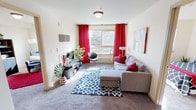 This single-floor unit at 4051 S 144th St in Tukwila, Washington, offers a well-organized layout with distinct living, sleeping, and functional zones. The living room serves as the heart of the space, featuring carpet flooring, a large window dressed with bold red curtains that invite natural light and views of surrounding greenery, and enough room to accommodate a sectional sofa and media setup comfortably.

The open transition between the living area and kitchen is defined by a shift to wood-style plank flooring, creating a natural delineation between spaces. The kitchen is efficiently designed with light wood cabinetry, ample counter space with white surfaces, and full-size appliances including a black refrigerator—providing practical functionality for daily use.

Two carpeted bedrooms offer restful retreats, each with windows overlooking outdoor scenery. The primary bedroom includes a sliding-door closet with built-in shelving, while the secondary bedroom is bright and simply appointed. An additional flex room with carpet and a window provides versatile space suitable for a home office or reading nook.

The full bathroom features wood-style flooring, a tub-shower combination, and a vanity with light cabinetry. Throughout the unit, neutral walls and consistent finishes create a cohesive and inviting atmosphere.