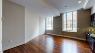 This single-floor urban residence offers a well-appointed layout that blends contemporary finishes with functional design throughout. The open living area is a standout, showcasing rich, deep-toned hardwood flooring that flows seamlessly through the main spaces, complemented by large windows that frame impressive city skyline views and flood the interior with natural light.

The kitchen is fully equipped for modern living, featuring a complete suite of stainless steel appliances — including a range, built-in microwave, dishwasher, and refrigerator — set against dark espresso cabinetry, granite countertops, and a distinctive striped tile backsplash. A dedicated built-in desk area with matching dark cabinetry and granite surfaces provides a practical workspace within the residence.

The bedroom offers plush carpeting and a generous window with urban views, creating a quiet and comfortable retreat. The bathroom is finished with warm travertine tile flooring and wall surround, a corner glass-enclosed shower, a dark vanity with granite countertop, and a well-placed mirror. Additional convenience is provided by an in-unit stacked washer and dryer, neatly tucked behind a panel door. Throughout the space, clean white millwork, crown molding details, and a neutral color palette contribute to a polished, cohesive aesthetic.