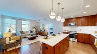This thoughtfully designed 2-bedroom, 2-bathroom residence offers a seamless open-concept floor plan that connects the kitchen, dining, and living areas into one cohesive and functional space. The kitchen is a standout feature, showcasing rich warm-toned wood cabinetry extending to the ceiling, stainless steel appliances, white subway tile backsplash, and a generous island with a quartz countertop illuminated by a trio of globe pendant lights — ideal for both meal preparation and casual dining. Hardwood flooring flows throughout the main living areas, adding warmth and continuity. The spacious living room benefits from large windows that invite abundant natural light and features clean, neutral walls that complement the open ambiance. The primary bedroom is a comfortable retreat, complete with access to a private balcony offering elevated outdoor views, while both bedrooms include dedicated closet space. The primary bathroom is finished with warm wood vanity cabinetry, a dual-sink countertop, and a glass-enclosed walk-in shower, all set on light tile flooring. The second bathroom includes a tub-shower combination with a similarly clean, modern finish. Two closets provide practical storage throughout the residence.