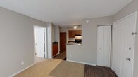 Located within the Town Brooke community in Middletown, Connecticut, this single-floor residence offers a practical and well-organized layout. The living area is spacious and open, featuring neutral-toned carpet that extends throughout most of the unit, warm gray walls, and a textured ceiling. Natural light filters in through a sliding glass door, brightening the entryway and main living space. A standard front door with dark wood flooring at the threshold provides a clear entry point, complemented by a closet nearby for convenient storage.

The kitchen is accessible via a pass-through counter that connects it to the living area, creating an open feel while maintaining defined zones. It is equipped with warm-toned wood cabinetry, dark granite-style countertops, and black appliances including a gas range with overhead ventilation and a full-size refrigerator. Wood-look flooring runs throughout the kitchen, adding a cohesive contrast to the carpeted living spaces.

The bedroom is generously sized with plush carpeting, a window allowing natural light, and a textured ceiling consistent with the rest of the unit. The bathroom features a full tub and shower combination enclosed by classic white square tile with a decorative accent stripe, chrome fixtures, and a granite-style vanity countertop with an oversized mirror.