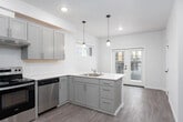 This contemporary multi-floor space is designed with a clean, modern aesthetic that emphasizes functionality and cohesive finishes throughout. The kitchen serves as a central highlight, featuring gray shaker-style cabinetry paired with white quartz countertops and a full suite of stainless steel appliances, including a refrigerator, electric range, and dishwasher. Pendant lighting accents the kitchen's peninsula, while recessed lighting and a window provide additional brightness to the space.

The living areas are finished with wood-style luxury vinyl plank flooring in a warm tone, carried consistently throughout the unit. One living space benefits from a large corner window arrangement, allowing generous natural light and outward views of the surrounding neighborhood. Additional rooms feature standard windows that bring in natural light while maintaining privacy.

The bathrooms echo the kitchen's design language, presenting gray vanity cabinetry with white countertops, wood-style flooring, and clean white surrounds. At least one bathroom includes a full soaking tub with a shower, while another offers a similar tub-and-shower combination. The overall palette of neutral whites, warm wood tones, and soft gray cabinetry creates a cohesive, move-in-ready environment across all three floors.