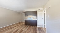 This single-floor unit offers a practical and modern layout designed for comfortable everyday living. Wood-look flooring flows throughout the space, providing a warm, cohesive aesthetic complemented by neutral beige walls and textured ceilings.

The open living and dining area is generously proportioned, anchored by a ceiling fan with light fixture and bathed in natural light from a large window with blinds. A front entry door with an adjacent window adds to the brightness and accessibility of the main living space.

The kitchen is a well-designed galley-style corridor, featuring dark espresso cabinetry on both sides, white countertops, a stainless steel sink, and a stylish linear mosaic tile backsplash. White appliances, including a range and refrigerator, are integrated neatly into the layout. A peninsula with matching dark cabinetry and an overhead cabinet separates the kitchen from the living area, offering a convenient pass-through and additional storage.

The bedroom is a comfortable retreat with its own ceiling fan, a window overlooking the outdoors, and direct access to both a walk-in closet with shelving and a full bathroom. The bathroom features tile surround walls and a combined tub and shower. A louvered closet door near the main living area provides additional storage options throughout the unit.