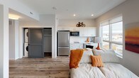This single-floor studio is a thoughtfully designed open-concept space that maximizes every square foot through a clean, modern aesthetic and smart layout. Wood-style plank flooring runs continuously throughout, unifying the living, sleeping, and kitchen areas into one cohesive environment. A large window brings in natural light and provides outdoor views, enhancing the sense of openness in the main living area.

The kitchen is outfitted with white cabinetry extending to the ceiling for ample storage, a stainless steel full-size refrigerator, a built-in microwave, a smooth-top electric cooktop, a dishwasher, and a single-basin sink. Light countertops complement the crisp white cabinetry for a modern, streamlined look.

The living and sleeping area occupies the open main space, where recessed and flush-mount lighting provide consistent illumination. A sliding louvered door conceals a dedicated closet, offering organized storage without disrupting the open feel.

The bathroom includes a full bathtub and shower combination with a curved curtain rod, a vanity with an undermount sink, gray-toned countertops, white cabinetry below, and built-in open shelving for additional storage. The overall design is neutral, contemporary, and efficiently planned.