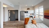 This single-floor studio is a thoughtfully designed open-concept space that maximizes every square foot through a clean, modern aesthetic and smart layout. Wood-style plank flooring runs continuously throughout, unifying the living, sleeping, and kitchen areas into one cohesive environment. A large window brings in natural light and provides outdoor views, enhancing the sense of openness in the main living area.

The kitchen is outfitted with white cabinetry extending to the ceiling for ample storage, a stainless steel full-size refrigerator, a built-in microwave, a smooth-top electric cooktop, a dishwasher, and a single-basin sink. Light countertops complement the crisp white cabinetry for a modern, streamlined look.

The living and sleeping area occupies the open main space, where recessed and flush-mount lighting provide consistent illumination. A sliding louvered door conceals a dedicated closet, offering organized storage without disrupting the open feel.

The bathroom includes a full bathtub and shower combination with a curved curtain rod, a vanity with an undermount sink, gray-toned countertops, white cabinetry below, and built-in open shelving for additional storage. The overall design is neutral, contemporary, and efficiently planned.