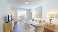 This thoughtfully designed single-floor residence offers a cohesive blend of comfort and contemporary style. The open-concept living and dining area is bathed in natural light from a large sliding glass door that leads to a private balcony with views of the surrounding community. Rich hardwood flooring runs throughout the main living spaces, complementing the warm, neutral color palette. A statement abstract canvas adds a pop of color to the living room, which features generous seating and a gold-accented coffee table.

The kitchen is well-equipped with dark espresso cabinetry, granite countertops, stainless steel appliances, and ample counter space on both sides of the galley-style layout, providing an efficient and stylish cooking environment. A pendant light adds a refined finishing touch.

The primary bedroom is a serene retreat with plush carpeting, a large tufted headboard, mirrored nightstands, and a bright window overlooking the exterior. The ensuite bathroom features a wide granite vanity with a dark wood base. A second bedroom offers similar comfort with large windows and soft carpeting. The second bathroom is equally well-finished, with hardwood flooring, a granite-topped vanity, and coastal-inspired décor throughout.