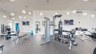 Located on Horizon Blvd in Athens, GA, this single-floor fitness center offers a spacious, thoughtfully designed exercise facility. The room features soaring ceilings that lend an open, airy atmosphere, complemented by oversized windows and glass doors that flood the space with natural light and provide sweeping views of the outdoor pool and surrounding grounds.

The facility is comprehensively equipped for a full-body workout. The cardio zone includes treadmills, elliptical machines, and a stair climber, all positioned along the large window wall to take advantage of the outdoor views. The strength training area features a cable machine system, a multi-functional power rack with a TKO punching bag, a flat weight bench, and a full dumbbell rack ranging across multiple weight increments, along with kettlebells and medicine balls. Dedicated selectorized machines for isolated muscle training are also present.

The flooring throughout is durable rubber gym matting, ideal for both heavy lifting and high-impact exercise. Spherical globe pendant lights hang from the high ceiling, adding a modern, clean aesthetic to the white walls. A water fountain is conveniently located within the space, and wall-mounted TVs provide entertainment. The fitness center's bright, modern design and comprehensive equipment make it a well-rounded facility for residents in Athens, GA.