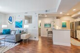 This single-floor residence offers a thoughtfully designed open-concept layout that seamlessly connects the living, dining, and kitchen areas. Rich hardwood flooring flows throughout the main living spaces, anchoring the bright, airy atmosphere created by recessed lighting and a ceiling fan overhead. The living room provides generous seating space and opens directly to a private patio through sliding glass doors, allowing abundant natural light and outdoor views. Adjacent to the living area, the dining space comfortably accommodates a round table and chairs, accompanied by a large window that looks out onto lush surroundings.

The galley-style kitchen is well-equipped with stainless steel appliances, including a gas range, microwave, refrigerator, and dishwasher. White cabinetry and granite-style countertops lend a clean, modern aesthetic, while a peninsula with bar seating creates a convenient pass-through to the main living area. An in-unit washer and dryer are conveniently located just off the kitchen.

Both bedrooms feature plush carpeting, ample natural light from windows with outdoor views, and ceiling fixtures. Each is served by a full bathroom finished with granite-topped white vanities, large-format tile tub-and-shower combinations, and built-in shelving for storage. The cohesive teal and neutral color palette throughout the residence creates a stylish and inviting ambiance.