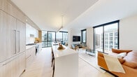 This contemporary residence offers a thoughtfully designed single-floor layout with four bedrooms and four bathrooms, delivering an expansive and light-filled living experience. The open-plan kitchen and living area serves as the heart of the home, anchored by a large waterfall-edge island with bar seating, sleek white cabinetry, warm wood accents, and a gas cooktop. Floor-to-ceiling windows frame sweeping city views and flood the space with natural light, while light-toned hardwood flooring flows seamlessly throughout. The living room is generously proportioned, featuring large glass panels on multiple sides that create an immersive connection to the urban skyline. The spacious primary bedroom benefits from dramatic corner glazing, offering panoramic outdoor views and an airy, retreat-like ambiance. Additional bedrooms are well-sized and bright, each with clean white walls and easy access to hallways and closet storage. The four bathrooms are finished to a high standard, featuring large-format tiles, floating vanities with under-lit mirrors, walk-in glass showers, and refined fixtures. Hallways are wide and well-lit, with additional natural light provided by window walls. Two dedicated closet spaces add to the home's practical storage. The overall aesthetic is clean, modern, and sophisticated.