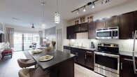 This well-appointed single-floor residence at 444 W Commerce St in Dallas, Texas offers a thoughtfully designed layout with modern finishes and a cohesive contemporary aesthetic throughout. The open-concept kitchen serves as a central focal point, featuring rich dark-espresso cabinetry, sleek dark countertops, a subway tile backsplash, and a full suite of stainless steel appliances including a range, microwave, and refrigerator. A large kitchen island with bar seating and stylish pendant lighting above creates an ideal space for both meal preparation and casual dining. Wood-style flooring flows throughout the main living areas, adding warmth and continuity to the design. The living room is bright and inviting, with large sliding glass doors that bring in natural light and provide access to an outdoor balcony with views of the surrounding area. A ceiling fan adds comfort to the space. The bedrooms are carpeted for a softer feel, each featuring windows that allow natural light and views of surrounding greenery. The bathroom includes a soaking tub with tile surround and wood-style flooring, maintaining the home's consistent, modern character. Track lighting and recessed fixtures throughout ensure well-lit spaces. The overall ambiance is contemporary and polished, blending functionality with refined style.