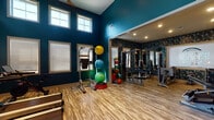 Located at 531 Old Maccumber Station Dr in Wilmington, NC, the Hawthorne Station fitness center is a well-appointed, single-floor workout facility designed to support a comprehensive range of exercise routines. The space is characterized by soaring vaulted ceilings and bold teal accent walls that create an energizing atmosphere, while rows of large windows along the perimeter flood the room with abundant natural light.

The main cardio area houses a lineup of treadmills, stationary bikes, an elliptical, and additional aerobic equipment, all positioned to take advantage of the natural light streaming through the windows. Durable wood-look flooring spans the entire facility, providing both style and functionality underfoot.

A dedicated strength and functional training zone features a full rack of dumbbells, cable machines, and resistance equipment. An adjacent room with striking dark herringbone-patterned accent walls and full-length mirrors contains specialty equipment, including a sophisticated targeting machine, a flat bench, and additional strength machines. This area also displays the Hawthorne Station branding prominently on a large framed mirror.

A separate section provides stability balls, medicine balls, a power rack, and other functional fitness tools, while a massage chair station offers a recovery amenity. Recessed lighting throughout enhances visibility in every corner, making this fitness center a polished and practical resource for residents.