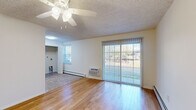 This single-floor unit offers a clean, functional layout highlighted by warm hardwood flooring that flows throughout the main living areas and bedrooms. The spacious living room is a standout feature, bathed in natural light streaming through large windows and a full-width sliding glass door fitted with vertical blinds, offering views of the surrounding greenery. A ceiling fan overhead and baseboard heating along the walls ensure year-round comfort, complemented by a wall-mounted air conditioning unit for warmer months. The textured ceilings are consistent throughout the unit, adding a classic residential character.

The kitchen is efficiently designed with white shaker-style cabinetry extending to the ceiling for ample storage, dark granite-style countertops, and a full suite of white appliances including a refrigerator, electric range, built-in microwave, and dishwasher. A louvered bifold door adjacent to the kitchen reveals a dedicated closet for additional storage.

The bedroom areas continue the hardwood flooring and ceiling fan theme, with generous natural light from windows and access to the hallway. The bathroom features tile flooring, a vanity with granite-style countertops, a medicine cabinet with mirror, and a clean, neutral palette throughout.