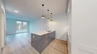 Located at 55 Riverside Dr in Yonkers, NY, this thoughtfully designed single-floor studio offers a bright and modern living experience. The open-plan layout maximizes every inch of the space, seamlessly connecting the kitchen and living areas. The kitchen is a standout feature, centered around a substantial island with a crisp white stone countertop and sleek gray cabinetry, accented by a trio of globe pendant lights with warm brass finishes that lend an elegant, contemporary touch. A stainless steel sink and full appliance suite complete the culinary space. Light wide-plank wood flooring runs throughout, contributing to a clean, airy aesthetic. Large floor-to-ceiling windows and glass-paneled doors flood the living area with natural light while framing views of the surrounding Yonkers neighborhood and lush greenery. The bathroom is finished with polished marble-look tile flooring, white subway tile walls, a marble-topped vanity, and brushed brass hardware for a refined feel. Two closets provide ample storage, and an in-unit laundry area adds everyday convenience. The space maintains a neutral, light-filled palette throughout, creating a calm and functional environment well-suited for modern urban living.