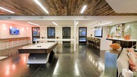 This single-floor recreational space combines modern industrial design with inviting social amenities. The open-concept layout is anchored by polished concrete floors that reflect the ambient lighting, creating a sleek and contemporary atmosphere throughout. A reclaimed wood plank ceiling adds warmth and texture, contrasting beautifully with the clean white structural columns and light stone-clad accent walls.

The space is designed for both entertainment and socializing. A full-size pool table serves as a central focal point in the main recreation area, complemented by additional game or lounge furnishings nearby. On the opposite side, a long communal bar counter is lined with high-back seating and illuminated by a cascading cluster pendant chandelier, making it an ideal spot for group gatherings.

Natural light filters in through multiple dark-framed windows positioned along the perimeter walls, offering a balanced and well-lit environment. Recessed linear LED lighting embedded in the ceiling enhances visibility while maintaining a refined aesthetic. The combination of raw materials, curated lighting, and purposeful layout gives this space a polished yet approachable character, well-suited for community events, casual entertainment, and social interaction.