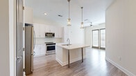 Located at 2001 Commerce St in Alpharetta, GA, this well-appointed one-bedroom, one-bathroom residence offers a thoughtfully designed single-level layout. The open-concept kitchen and living area serves as the heart of the home, showcasing light wood-look flooring, white shaker cabinetry extending to the ceiling, and a full suite of stainless steel appliances including a french door refrigerator, range, and built-in microwave. A central island with a light quartz countertop, undermount sink, and elegant pendant lighting provides both additional prep space and a natural gathering spot. Double glass doors in the living area invite natural light and offer access to the outdoors. The bedroom features soft carpeting, a ceiling fan, and direct access to a dedicated walk-in closet equipped with multi-tier wire shelving for generous storage. The bathroom is finished with large-format tile flooring, a white vanity with quartz countertop, a wide frameless mirror, and a full tub-shower combination accented with decorative tile inlay. Neutral tones and clean architectural lines throughout create a bright, cohesive ambiance well-suited to everyday living in the heart of downtown Alpharetta.