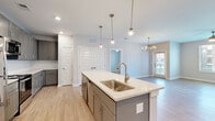 This contemporary single-floor residence is designed with a clean, modern aesthetic and a thoughtful open-concept layout. The heart of the home is the kitchen, which features gray shaker-style cabinetry, light quartz countertops, a subway tile backsplash, stainless steel appliances, and a generously sized center island with an undermount sink and pendant lighting overhead. The kitchen flows seamlessly into the living area, which is brightened by natural light from a large window and accented by a stylish chandelier, creating a warm and welcoming gathering space. Light wood-tone flooring runs consistently throughout the residence, enhancing the sense of openness and continuity. The bedrooms are comfortably sized, each featuring ceiling fans, ample natural light, and well-organized closets with built-in shelving. The primary bathroom includes gray vanity cabinetry with quartz countertops, an undermount sink, brushed nickel fixtures, and access to a walk-in closet. A secondary bathroom offers a tiled tub-shower combination with neutral large-format tile and matching brushed nickel hardware. Additional storage is provided throughout, including a pantry area adjacent to the kitchen. The overall ambiance is fresh, clean, and move-in ready, with consistent finishes that lend a cohesive, polished look across every room.