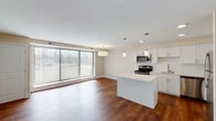 Located at 12215 Huffman Rd in Parma Heights, Ohio, this single-floor residence offers a thoughtfully designed open-concept layout that seamlessly connects the living and kitchen areas. Rich hardwood flooring flows throughout the main living space, complementing the neutral, warm-toned walls and creating a cohesive, inviting atmosphere.

The kitchen is a standout feature, outfitted with crisp white shaker-style cabinetry, a classic subway tile backsplash, and light-toned quartz countertops. A central island with a matching quartz surface provides additional workspace and casual seating. Stainless steel appliances — including a range, microwave, dishwasher, and refrigerator — complete the functional and modern aesthetic. Pendant lighting above the island adds focused illumination and a refined touch.

The living area benefits greatly from a large picture window fitted with vertical blinds, allowing generous natural light to fill the space while offering views of the surrounding outdoor environment. Closet storage is conveniently accessible from the main living zone.

The bathroom features neutral tile work, a soaking tub with shower combination, a white vanity with ample storage, and clean, understated finishes throughout. The overall design of this residence balances modern updates with a comfortable, practical layout.