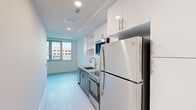 This thoughtfully designed two-bedroom, one-bathroom unit makes efficient use of its compact footprint across a single floor. The layout flows from a dedicated entrance corridor into the galley-style kitchen, which serves as a design highlight. The kitchen features granite countertops, stainless steel appliances including a full-size refrigerator and range with oven, a stainless steel undermount sink, white subway tile backsplash, and a combination of white upper cabinetry and sleek gray lower cabinets with brushed nickel hardware. Recessed lighting keeps the space bright throughout.

Light-toned hardwood-style flooring runs consistently throughout the unit, contributing to a clean, cohesive aesthetic. The primary bedroom accommodates essential furnishings and benefits from a large window framing open outdoor views of the surrounding neighborhood. The second bedroom is bright and simply finished with clean white walls. A dedicated closet includes a stacked washer and dryer alongside built-in shelving, adding practical storage and in-unit laundry convenience. The bathroom is finished with white subway tile surrounding a full soaking tub and shower combination, a granite-topped vanity, and brushed nickel fixtures, maintaining the unit's consistent modern design language.
