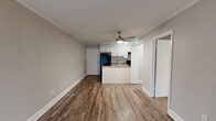 Located at 2360 West Broad Street in Athens, GA, this one-bedroom, two-bathroom unit offers a functional and well-appointed layout across a single floor. The open-concept living and kitchen area serves as the heart of the home, featuring durable hardwood-style flooring, crown molding, and a ceiling fan with light fixture. The kitchen is equipped with white cabinetry, granite-style countertops, a peninsula breakfast bar, a stainless steel sink, and black appliances including a refrigerator and range. Built-in shelving in the living area adds character and storage, while a sliding glass door floods the space with natural light and provides direct access to a private balcony. The bedroom is carpeted for comfort, includes a ceiling fan, and is served by two full bathrooms — one featuring a vanity with granite-style countertops and wood-look flooring, and the other featuring a full tub-shower combination with white tile surround. Textured walls throughout lend a distinct character to each room, while clean white baseboards and trim provide a crisp, cohesive finish. A hallway connects the private spaces, completing this efficient and practical layout.
