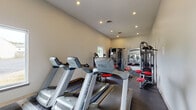 Located at 3099 Kirklevington Drive in Lexington, Kentucky, this fitness center offers a compact yet comprehensively outfitted space designed to support a full range of workout routines. The room features a dark rubberized flooring, neutral-toned walls, and a ceiling lined with recessed lighting that ensures bright, even illumination throughout.

The cardio section is anchored by a row of Matrix treadmills and elliptical cross-trainers, positioned to make efficient use of the available floor space. A window along the wall allows natural light to filter in and provides a view of the surrounding outdoor area. On the strength training side, the space is equipped with multiple selectorized cable and weight machines featuring red upholstered seats, a multi-functional cable tower, and a dedicated free weight area. The free weight station includes a tiered dumbbell rack stocked with a range of weights, stability balls, and exercise mats, all positioned in front of a large wall-mounted mirror that enhances the sense of openness.

The overall layout is practical and well-organized, allowing users to move between cardio and strength equipment with ease. The clean, functional design makes this fitness center a convenient and capable amenity for those seeking a structured exercise environment.