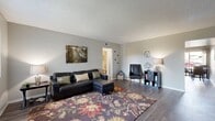 This thoughtfully designed single-floor residence offers a comfortable and functional layout across six distinct spaces. The spacious living room features rich hardwood-style flooring, neutral gray walls, and a textured ceiling, creating a welcoming atmosphere ideal for relaxing or entertaining. A floating wall shelf adds a subtle decorative touch near the front entry.

The galley-style kitchen is bright and efficient, outfitted with white cabinetry, light stone countertops, a gas range, dishwasher, and a double sink — all complemented by wood-look flooring that ties seamlessly into the adjacent dining area. The dining space benefits from a ceiling fan and a sliding glass door that opens to a private balcony, filling the room with natural light and outdoor access.

The bedroom is a calm retreat, featuring a window with natural light, textured ceiling, and the same warm hardwood-style flooring found throughout. A separate office provides a dedicated workspace with its own window, wall-mounted shelving, and light-toned flooring. Both bathrooms are finished with white cabinetry, stone-look countertops, large vanity mirrors, and brushed nickel fixtures. A hallway connects all areas, contributing to the home's cohesive and practical flow.