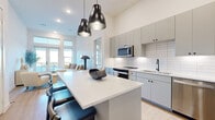 Located at 900 E Colorado Blvd in Dallas, TX, this well-designed 2-bedroom, 2-bathroom home offers a thoughtful single-floor layout with modern finishes throughout. The open-concept kitchen is a standout feature, showcasing gray flat-front cabinetry, a white subway tile backsplash, stainless steel appliances, and a generous quartz waterfall island with bar seating — all illuminated by a pair of striking black pendant lights. The kitchen flows seamlessly into the living area, which benefits from abundant natural light through large glass doors that open to a balcony with outdoor views. The primary bedroom is a comfortable retreat with windows framing a serene tree-lined view, while three closets — including a walk-in — provide ample storage throughout the home. The primary bathroom features a double vanity with warm wood cabinetry, matte black hardware, an illuminated mirror, and a glass-enclosed walk-in shower with white tile. Wide-plank wood-look flooring runs through the main living areas, complemented by neutral tones that create a clean, contemporary ambiance. An in-unit laundry closet with a full-size Whirlpool washer and dryer adds everyday convenience to this polished Dallas residence.