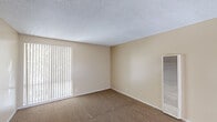Unit #217 at 145-149 Canyon in Oceanside is a single-floor residence designed with a functional, straightforward layout. The living area is finished with neutral-toned carpet and warm beige walls, creating a clean and understated atmosphere. Vertical blinds on a large window allow for adjustable natural light while offering views of surrounding greenery. A wall-mounted heating unit provides in-unit climate control, and the textured ceiling adds a classic touch consistent throughout the space.

A hallway connects the main living area to the rest of the unit, transitioning from carpet to wood-look flooring as it leads toward the kitchen and bathroom. The kitchen is equipped with white cabinetry, a gas range, and a curved breakfast bar that provides casual dining or prep space. The bathroom features a full tub-shower combination, a vanity with a speckled countertop, a mirrored medicine cabinet, and wood-look flooring that complements the rest of the unit.

The bedroom offers carpeted flooring, a ceiling light fixture, and a window with vertical blinds that allows in natural light. The overall ambiance of the unit is neutral and practical, providing a comfortable and move-in-ready living environment in Oceanside.