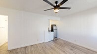 Located at 4451 Lockwood Ave in the East Hollywood neighborhood of Los Angeles, this studio unit offers an efficiently designed single-floor layout. The combined kitchen and living area serves as the heart of the space, finished with light hardwood-style flooring that extends throughout and crisp white walls that maximize the sense of openness. A ceiling fan with an integrated light fixture provides both ventilation and ambient lighting. The kitchenette is neatly tucked into a recessed alcove and is equipped with a refrigerator, microwave, and sink, keeping the living area open and unobstructed. A large window allows natural light to pour in, offering a view of surrounding greenery and brightening the interior. Two doors along one wall lead to a closet and utility access, keeping storage and mechanical elements discreetly out of sight. The bathroom features a clean, all-white design with a full-size soaking tub, a rain showerhead with a handheld attachment, polished chrome fixtures, and white cabinetry. The overall aesthetic is minimal and modern, with a neutral palette throughout that makes the space feel bright, clean, and move-in ready.