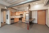 This single-floor loft-style unit showcases a compelling blend of industrial and modern design elements throughout. Exposed concrete ceilings and visible ductwork lend an authentic urban character to the space, while large floor-to-ceiling windows flood the interior with natural light and offer sweeping elevated views of the surrounding landscape and cityscape below.

The kitchen is a functional and well-appointed space, featuring light maple cabinetry with ample upper and lower storage, stainless steel appliances including a refrigerator, range, microwave, and dishwasher, complemented by a stainless steel countertop and a tiled backsplash. A built-in counter with bold red hairpin legs serves as a casual dining or workspace area just adjacent to the kitchen, enhanced by pendant lighting overhead. Track lighting runs along the ceiling, providing flexible illumination throughout.

The bathroom is clean and efficiently designed, with a wood-toned vanity, dark countertop, and well-lit mirror. A stacked washer and dryer unit is conveniently integrated into the bathroom, adding in-unit laundry functionality. Polished concrete floors carry through the space, reinforcing the industrial character while remaining easy to maintain. The overall ambiance is modern, open, and distinctly loft-inspired.