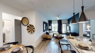 Located in Richmond, TX, this single-story residence showcases a thoughtfully designed open-concept layout that seamlessly connects the living, dining, and kitchen areas. Light wood-style flooring flows throughout, complementing the crisp white walls and bold navy accent walls that add depth and character to the space.

The living area is anchored by a tufted sectional sofa and dressed with distinctive woven wall art and textured mirror frames, creating a warm yet contemporary ambiance. Natural light pours in through large windows dressed with layered blinds and floor-to-ceiling dark curtains. The adjacent dining area features a hexagonal wooden table with seating for four, set beneath a sculptural sunburst mirror.

The kitchen is equipped with slate-gray cabinetry, granite countertops, a full suite of stainless steel appliances, tile backsplash with under-cabinet lighting, and a built-in wine rack — offering both style and functionality.

The bedroom is a serene retreat with a muted gray accent wall, large windows with outdoor views, wood-toned dresser, and curated wall art. The bathroom features marble-style tiled tub surround, granite vanity countertop, and coordinating gray cabinetry, delivering a cohesive, polished aesthetic throughout.