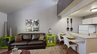 This two-floor, one-bedroom, one-bathroom residence is thoughtfully designed to maximize every square foot across its two levels. The main floor opens into a combined living, dining, and kitchen area. The living room features soaring vaulted ceilings that create an impressive sense of vertical space, with soft carpeting underfoot and large windows fitted with shutters that allow generous natural light while maintaining privacy. A defined dining area sits adjacent to the living space, flowing seamlessly into the galley-style kitchen. The kitchen is equipped with white cabinetry, laminate countertops, a double sink, dishwasher, range, and full-size refrigerator, all set over warm hardwood-style flooring. A full bathroom on this level includes a single-sink vanity with a wide countertop and a shower/tub combo. The upper floor is dedicated entirely to the spacious primary bedroom, which benefits from dramatic angled ceilings and a prominent skylight that floods the room with natural light and outdoor tree views. The bedroom includes a built-in closet with dual hanging rods and is finished with plush carpeting. Together, the two floors deliver an efficient and characterful layout well-suited for comfortable everyday living.