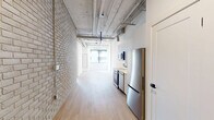 Located at 685 Richmond Street in the heart of London, Ontario, this two-bedroom, one-bathroom unit offers a distinctive industrial-chic aesthetic with thoughtful modern finishes throughout. The open-concept living and kitchen area is anchored by exposed ductwork and piping along the ceiling, which lends the space a loft-like character. A whitewashed brick accent wall adds texture and warmth, while light hardwood flooring runs throughout, creating a cohesive and airy feel. The kitchen is outfitted with stainless steel appliances, including a built-in range and over-the-range microwave, complemented by crisp white cabinetry. Large, black-framed windows flood the living area and both bedrooms with abundant natural light, offering views of the surrounding urban cityscape and greenery. The primary bedroom provides a comfortable retreat with its own oversized window, while the second bedroom mirrors this brightness with a similarly generous window and clean-lined walls. The bathroom features a sleek, minimalist design with a wall-mounted vanity, black-accented fixtures, a framed mirror, and light tile flooring. Two hallways provide practical circulation throughout the unit. This well-appointed space combines urban character with contemporary convenience in a central London location.