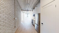 Located at 685 Richmond Street in the heart of London, Ontario, this two-bedroom, one-bathroom unit offers a distinctive industrial-chic aesthetic with thoughtful modern finishes throughout. The open-concept living and kitchen area is anchored by exposed ductwork and piping along the ceiling, which lends the space a loft-like character. A whitewashed brick accent wall adds texture and warmth, while light hardwood flooring runs throughout, creating a cohesive and airy feel. The kitchen is outfitted with stainless steel appliances, including a built-in range and over-the-range microwave, complemented by crisp white cabinetry. Large, black-framed windows flood the living area and both bedrooms with abundant natural light, offering views of the surrounding urban cityscape and greenery. The primary bedroom provides a comfortable retreat with its own oversized window, while the second bedroom mirrors this brightness with a similarly generous window and clean-lined walls. The bathroom features a sleek, minimalist design with a wall-mounted vanity, black-accented fixtures, a framed mirror, and light tile flooring. Two hallways provide practical circulation throughout the unit. This well-appointed space combines urban character with contemporary convenience in a central London location.