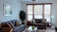 Located at 549 Avenida Sexta in Clermont, Florida, this single-floor residence offers a thoughtfully designed layout with comfortable living spaces throughout. The living room serves as the heart of the home, featuring large windows dressed with blinds and curtains that allow ample natural light to fill the space. A ceiling fan overhead and soft carpeted flooring contribute to a relaxed atmosphere, while the open layout provides generous room for seating arrangements. The galley-style kitchen is efficiently arranged with warm wood cabinetry lining both walls, light countertops, tile flooring, and white appliances including a range, microwave, refrigerator, and dishwasher. A breakfast bar with seating extends from the kitchen, creating a convenient casual dining area. The bedroom is a serene retreat with plush carpeting, multiple windows for natural light, a ceiling fan, and a private door offering direct outdoor access. The bathroom features tile flooring, a wood vanity with an extended countertop, and a large mirror. Completing the unit is an in-unit laundry area equipped with a full-size washer and dryer tucked behind bi-fold doors, adding practical convenience to everyday living.