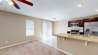 This three-floor home offers a thoughtfully organized layout across three distinct levels, providing generous living space for everyday comfort. The ground floor houses a garage with a standard roll-up door and concrete flooring, offering secure parking and additional storage. The main living level features an open-concept area that combines the kitchen, dining, and living room into one cohesive space. The kitchen is equipped with stainless steel appliances, including a range, microwave, and refrigerator, complemented by dark espresso cabinetry and a granite-topped breakfast bar. Neutral-toned carpet flows through the living area, while tile flooring defines the kitchen zone. A sliding glass door and side window invite natural light and outdoor access. The upper floor is home to three bedrooms, including a spacious primary suite, along with three closets and multiple bathrooms. Each bathroom features tile flooring, dark wood vanities with granite countertops, and glass-enclosed showers. A dedicated laundry room with side-by-side washer and dryer units and overhead cabinetry adds everyday convenience. Consistent warm beige tones, ceiling fans, and textured ceilings create a cohesive, practical ambiance throughout.