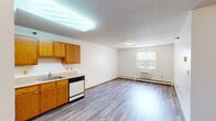 This single-floor unit offers a functional and accessible layout with consistent laminate wood-look flooring throughout. The open-concept living and kitchen area forms the heart of the space, providing a generous, versatile area for daily living. The kitchen is equipped with warm-toned oak cabinetry offering ample storage, a white refrigerator, an electric coil range with overhead ventilation, a dishwasher, and a single-basin sink. Light-toned countertops complement the cabinetry, creating a cohesive look. A fluorescent overhead fixture illuminates the kitchen, while the living area benefits from natural light through a window fitted with vertical blinds. Baseboard heating and a wall-mounted air conditioning unit ensure year-round climate control. The bedroom is a well-proportioned room with its own window, baseboard heating, and direct access to additional spaces including a closet and bathroom. The bathroom is designed with accessibility in mind, featuring stainless steel grab bars positioned near the toilet for added safety. White walls and wood-toned trim are consistent throughout, contributing to a clean, neutral interior that provides a practical and comfortable living environment.