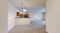 This single-floor residence offers a practical and functional layout across three bedrooms and two full bathrooms. The combined kitchen and living area forms the heart of the unit, where a peninsula-style counter with dark countertops separates the kitchen from the carpeted living space. The kitchen features warm medium-toned wood cabinetry, black appliances including a refrigerator and range, and hardwood-style flooring. A chandelier-style pendant light fixture adds a decorative touch above the peninsula. The living area extends toward French doors that invite natural light and provide outdoor access.

The primary bedroom is a comfortably sized room equipped with a ceiling fan and a walk-in closet outfitted with wire shelving and hanging rods for organized storage. The two additional bedrooms are carpeted and each features windows with outdoor views of the surrounding neighborhood. Both bathrooms include tile flooring and a tub-shower combination. A dedicated in-unit laundry room accommodates a full-size washer and dryer with overhead wire shelving for added storage. Neutral wall tones and consistent carpeting throughout the living spaces give the unit a clean, cohesive appearance.