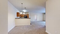 This single-floor residence offers a practical and functional layout across three bedrooms and two full bathrooms. The combined kitchen and living area forms the heart of the unit, where a peninsula-style counter with dark countertops separates the kitchen from the carpeted living space. The kitchen features warm medium-toned wood cabinetry, black appliances including a refrigerator and range, and hardwood-style flooring. A chandelier-style pendant light fixture adds a decorative touch above the peninsula. The living area extends toward French doors that invite natural light and provide outdoor access.

The primary bedroom is a comfortably sized room equipped with a ceiling fan and a walk-in closet outfitted with wire shelving and hanging rods for organized storage. The two additional bedrooms are carpeted and each features windows with outdoor views of the surrounding neighborhood. Both bathrooms include tile flooring and a tub-shower combination. A dedicated in-unit laundry room accommodates a full-size washer and dryer with overhead wire shelving for added storage. Neutral wall tones and consistent carpeting throughout the living spaces give the unit a clean, cohesive appearance.