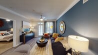 This thoughtfully designed single-floor residence combines contemporary style with practical comfort across a well-organized layout. The living room serves as the focal point of the home, showcasing a striking deep teal accent wall adorned with a decorative sunburst mirror, crown molding, a ceiling fan, and wood-look flooring. A full-glass door allows natural light to pour in while offering outdoor views, enhancing the open and airy ambiance of the space.

The kitchen is outfitted with stainless steel appliances, including a refrigerator, electric range, microwave, and dishwasher. Two-tone cabinetry — white uppers and gray lowers — pairs with a classic subway tile backsplash and light countertops for a clean, modern aesthetic.

The primary bedroom continues the teal accent wall motif, featuring a ceiling fan, plush carpeting, and generous natural light from a large window with blinds and drapes. A second bedroom provides additional living space, also carpeted and well-lit with outdoor-facing windows.

Two bathrooms echo the home's modern sensibility, each featuring gray vanity cabinetry, quartz-style countertops, wood-framed mirrors, and wood-look flooring. A dedicated in-unit laundry closet with a full-size washer and dryer adds everyday convenience, completing this well-appointed residence.