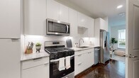 This thoughtfully designed single-floor residence showcases a cohesive modern aesthetic throughout its well-appointed spaces. The kitchen is a standout feature, outfitted with high-gloss white cabinetry extending to the ceiling for generous storage, granite countertops, a classic white subway tile backsplash, and a full suite of stainless steel appliances including a gas range, over-the-range microwave, dishwasher, and French door refrigerator. Rich, polished concrete flooring runs through the kitchen, adding an industrial-chic contrast to the crisp white finishes and under-cabinet lighting.

The bedroom is a serene retreat, featuring vaulted ceilings, warm neutral tones, and large windows that invite abundant natural light and offer views of a landscaped courtyard. The living area complements the bedroom's relaxed atmosphere, with additional windows framing outdoor greenery.

The bathroom maintains the home's clean design language, with large-format porcelain tile flooring, a white vanity topped with granite, and a glass-enclosed shower. Bright white walls and recessed lighting create an airy, spa-like feel. Together, these spaces deliver a refined, contemporary living environment with careful attention to detail and finish quality throughout.