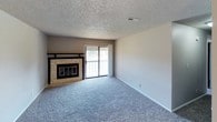 This single-floor residence is thoughtfully laid out across several functional spaces. The living area is generously sized, finished with plush carpet and a textured ceiling, and anchored by a tile-surround fireplace. A sliding glass door beside the fireplace opens to a balcony, filling the room with natural light and providing outdoor access. The space flows toward a dining or secondary living area, also carpeted, with a ceiling fan and open sightlines to the kitchen.

The galley-style kitchen features rich wood cabinetry extending to the upper walls, light countertops, a tile backsplash, and a stainless steel sink. A black electric range with overhead ventilation hood and a full-size refrigerator complete the appliance suite. A tall window centered at the end of the kitchen brightens the workspace with natural light.

The bedrooms are carpeted and equipped with ceiling fans with light fixtures, and each includes windows for ventilation and daylight. One bedroom offers direct access to a private bathroom and a walk-in closet, providing a practical en-suite arrangement. The bathroom includes a shower/tub combo and wood-toned cabinetry with a vanity mirror, maintaining a consistent design language throughout the unit.