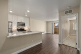 This single-floor residence offers a thoughtfully designed open-concept layout that connects the kitchen and living areas into one cohesive space. The kitchen serves as a central hub, anchored by a granite-topped island with an undermount sink and a gooseneck faucet, providing ample prep and casual dining space. White shaker-style cabinetry lines the walls and extends to the ceiling, offering generous storage, while a full suite of stainless steel appliances — including a refrigerator, gas range, and built-in microwave — adds a modern, functional edge. Recessed lighting illuminates the space throughout. Wood-look flooring runs through the kitchen and living areas, lending warmth and continuity, while the living room benefits from a sliding glass door that opens to a private balcony with outdoor views and abundant natural light. The bedroom features plush carpeting, a ceiling fan with light fixture, a closet with sliding mirrored doors, and a window with natural greenery views. The bathroom presents a white vanity with a granite countertop, an undermount sink, and mirrored medicine cabinets, with direct access to the bedroom and closet area creating a practical, connected layout.