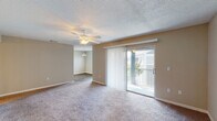 This single-floor residence offers a well-organized layout connecting living, dining, kitchen, and bedroom spaces through a carpeted hallway accented by wall sconces. The spacious living area features plush carpeting, a ceiling fan with light fixture, and a textured ceiling. A sliding glass door with vertical blinds opens to a balcony, allowing natural light to fill the room. An adjoining area, also ceiling fan-equipped, provides additional flexible living or dining space.

The kitchen is outfitted with white shaker-style cabinetry, granite-look countertops, a subway tile backsplash, stainless steel appliances including an electric range and dishwasher, and wood-look flooring. Two bathrooms serve the unit, each featuring granite-topped white vanities and wood-look flooring; one includes a shower-tub combination, while the other offers a dedicated vanity area. Both bedrooms are carpeted and include ceiling fans, windows with blinds, and generous closet storage — one bedroom features a walk-in closet, while another includes dual reach-in closets. Neutral tones and textured ceilings carry throughout, creating a cohesive and functional living environment.