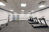 Located at 1850 Post Rd in Warwick, Rhode Island, this fitness center offers a well-equipped, single-floor exercise facility designed to support a wide range of workout routines. The space is generously sized, providing ample room for movement between equipment zones without feeling crowded.

The main cardio area features multiple Spirit-brand treadmills and elliptical trainers arranged in a row, allowing for comfortable side-by-side use. Adjacent to this section, a dedicated strength and functional training zone houses a multi-station cable and weight machine, a dumbbell rack with a full range of free weights, kettlebells, parallette bars, and a stability ball with accessories on a mobile cart. Wall-mounted foam roller and resistance band racks add to the functional training offerings.

A large mirror spans one wall of the strength area, enhancing the sense of space and supporting form-checking during workouts. The flooring throughout is dark rubber gym tile, providing traction and impact absorption. Walls are finished in crisp white with a navy accent stripe running the perimeter, lending a clean, professional aesthetic. The drop ceiling is fitted with recessed LED panel lighting that evenly illuminates the entire floor.

Access is provided through multiple doorways, including a set of glass double doors. The facility is well-ventilated with ceiling-mounted HVAC vents throughout.