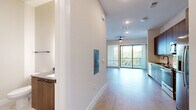 This single-floor unit presents a clean, contemporary design throughout, highlighted by light wood-tone flooring that flows seamlessly from room to room. The open-concept living area is bright and airy, benefiting from large sliding glass doors that lead to a private balcony overlooking lush tree canopy views. A ceiling fan adds functional comfort to the space, while recessed lighting provides consistent illumination.

The kitchen is well-appointed with warm wood cabinetry extending to the ceiling for ample storage, complemented by grey quartz countertops, a white subway tile backsplash, and a matte black faucet over a stainless steel sink. A full suite of stainless steel appliances includes a refrigerator with ice and water dispenser, an electric range, built-in microwave, and dishwasher.

The bedroom is generously proportioned, featuring a ceiling fan, natural light from a large window, sliding glass door access to the balcony, and a double-door closet. The bathroom offers a soaking tub with full-height neutral tile surround and matte black fixtures, maintaining the unit's consistent modern aesthetic throughout.