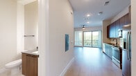 This single-floor unit presents a clean, contemporary design throughout, highlighted by light wood-tone flooring that flows seamlessly from room to room. The open-concept living area is bright and airy, benefiting from large sliding glass doors that lead to a private balcony overlooking lush tree canopy views. A ceiling fan adds functional comfort to the space, while recessed lighting provides consistent illumination.

The kitchen is well-appointed with warm wood cabinetry extending to the ceiling for ample storage, complemented by grey quartz countertops, a white subway tile backsplash, and a matte black faucet over a stainless steel sink. A full suite of stainless steel appliances includes a refrigerator with ice and water dispenser, an electric range, built-in microwave, and dishwasher.

The bedroom is generously proportioned, featuring a ceiling fan, natural light from a large window, sliding glass door access to the balcony, and a double-door closet. The bathroom offers a soaking tub with full-height neutral tile surround and matte black fixtures, maintaining the unit's consistent modern aesthetic throughout.