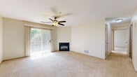 Located at 446 Danbury Ct in Copley, Ohio, this two-floor home offers a comfortable and functional layout designed for everyday living. The main living area is generously sized, featuring plush wall-to-wall carpeting, a ceiling fan with light fixture, and a corner fireplace that serves as a warm focal point. A sliding glass door with vertical blinds floods the room with natural light and provides access to the outdoors. A unique octagonal accent window adds architectural character to the space. The kitchen is equipped with white cabinetry, ample counter space, and stainless steel appliances including a refrigerator, range, and over-the-range microwave. Stone-look tile flooring grounds the kitchen with a practical yet attractive finish. Two full bathrooms are present, each featuring a tub-shower combination, white vanity, and the same earth-toned tile flooring for a cohesive aesthetic. Carpeted stairs with white trim and a handrail connect the two floors, continuing the home's neutral, light-filled palette throughout. A spacious walk-in closet with wire shelving provides generous storage. Overall, the home presents a clean, move-in-ready atmosphere with consistent warm neutral tones throughout.