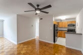 This single-floor residence is defined by its warm, polished parquet wood flooring, which extends consistently through the living areas and bedrooms, lending a cohesive and classic character to the space. The open-concept living and dining area is generously proportioned, featuring a ceiling fan with integrated lighting and neutral-toned walls that create a clean, versatile backdrop. A hallway connects the living area to the private rooms, maintaining an efficient and functional layout.

The kitchen is positioned adjacent to the main living area and is equipped with warm honey-toned wood cabinetry, dark granite-style countertops, and a full suite of black appliances including a refrigerator, gas range, dishwasher, and built-in microwave. Light ceramic tile flooring grounds the kitchen, providing a practical contrast to the parquet found elsewhere.

The bedrooms continue the parquet flooring theme and include sliding mirrored closet doors that add depth and reflect natural light. The primary bedroom benefits from a large window with vertical blinds, allowing for ample natural light and outdoor views. Additional bedrooms are well-sized with similar closet configurations. The bathroom features a tub-shower combination, tile surround, ceramic tile flooring, a wood vanity, and a wall-mounted mirror.